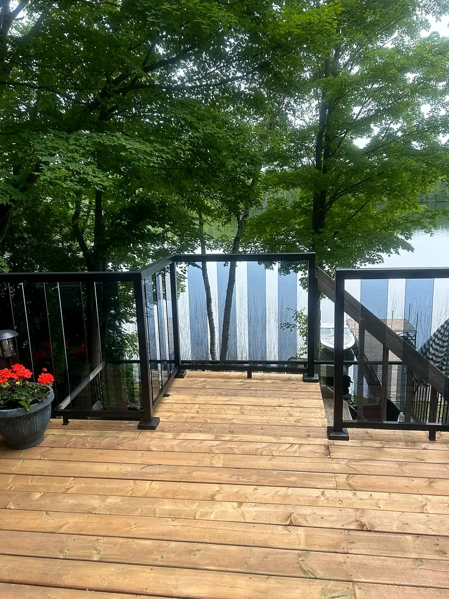Wooden deck with black aluminium railing looking out over a lake through trees