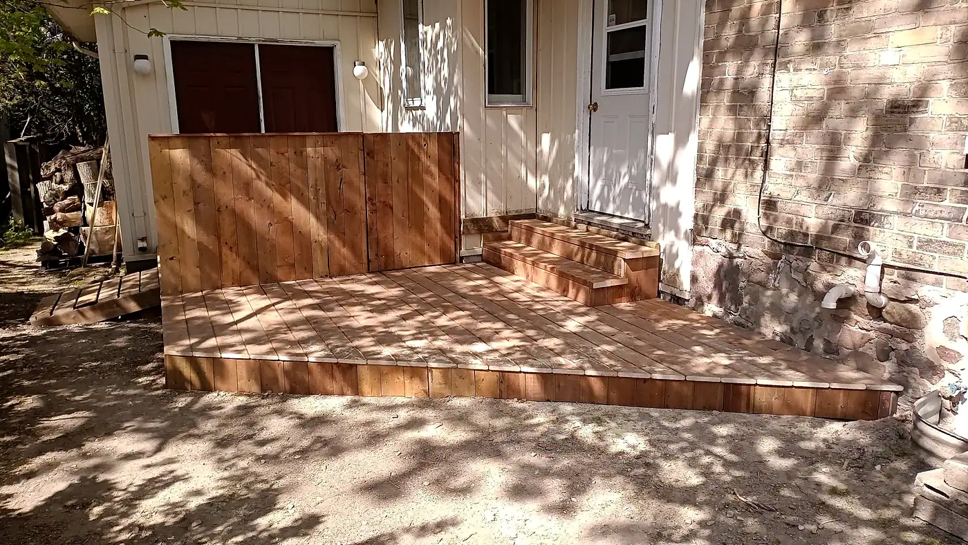 Partly finished wooden deck with newly built steps against the back of a house