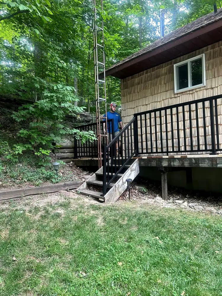 Raised wooden deck with black railings and a flight of stairs leading down to a lawn