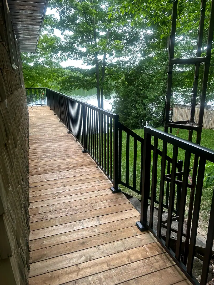 Long raised wooden walkway with black railing leading down toward a lake