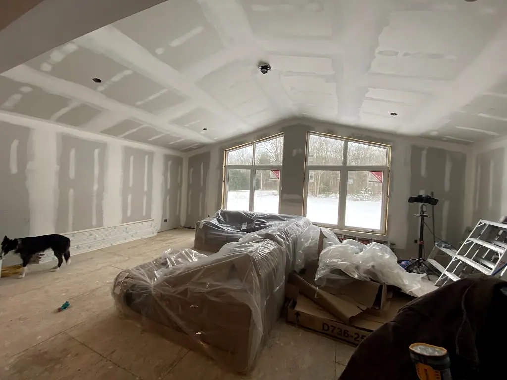 Great room with a vaulted drywall ceiling and a wall of windows, taped and sanded ready for paint