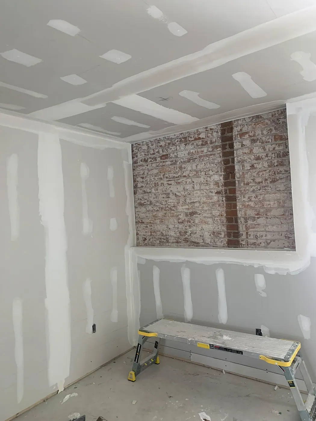 Drywalled room with taped joints framing an exposed original brick chimney